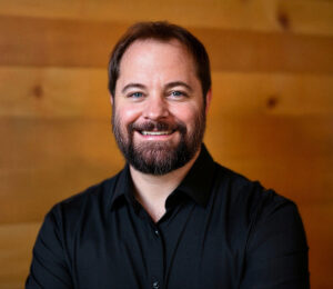 Picture of Pastor Stephen Vesolich smiling and standing in front of a wood panel.